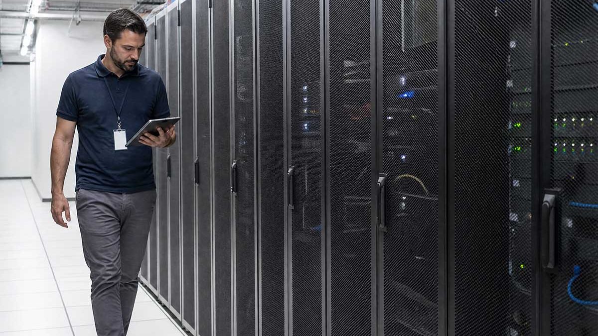 Técnico com tablet caminhando entre racks de servidores em um data center