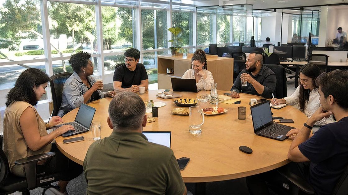 Equipe reunida em uma mesa de trabalho, cada pessoa com seu notebook