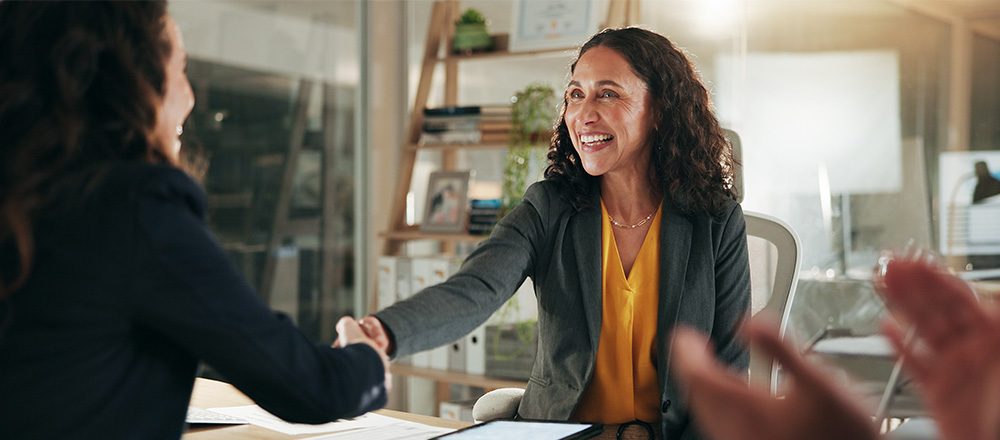 Profissional sorrindo e apertando a mão de uma cliente em uma reunião