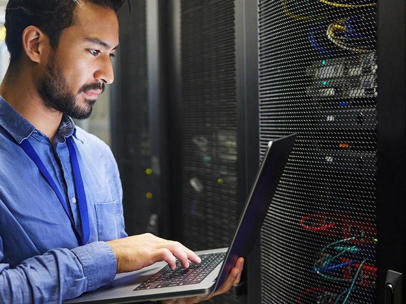 Profissional com notebook ao lado de racks de servidores